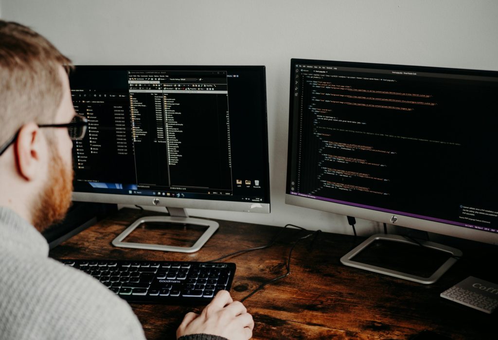 Software developer working on code with dual monitors in a home office setting.