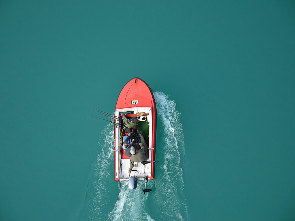 Top view of a red motorboat with fishermen navigating open turquoise waters.